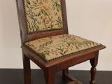 une vieille chaise en bois dont l'assise est recouverte d'un tissu à motifs floraux, posée sur une surface noire