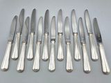 six silverplated knives and six knives on a white surface
