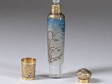 a small glass bottle with a bird on it next to a shot glass