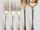 cinq fourchettes et deux cuillères sur une table blanche