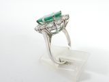 an emerald and diamond ring on display on a clear acrylic stand