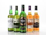 Quatre bouteilles de différents types de whisky sont alignées sur une surface blanche
