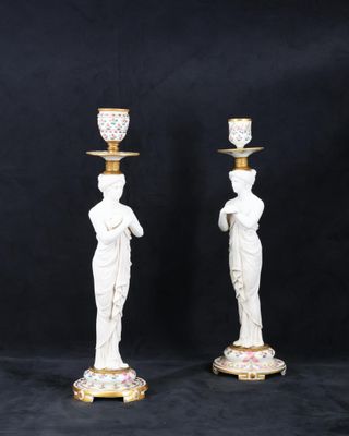 une paire de bougeoirs blancs et dorés ornés de statuettes