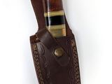 un étui en cuir marron sur lequel repose un couteau, posé sur une surface blanche
