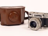 un appareil photo marron et un étui marron posés sur une surface blanche
