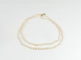 un collier de perles blanches avec un fermoir en or sur fond blanc