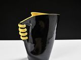 a black vase with a yellow handle on a white table