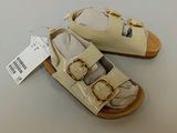 pair of baby shoes with gold buckles and a tag on a white surface