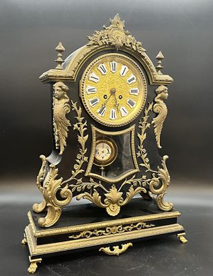 une horloge noire et dorée surmontée d'un oiseau