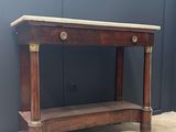 une vieille table en bois avec un plateau en marbre, posée sur un sol en béton