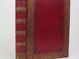 un vieux livre avec une couverture rouge et des bordures dorées sur fond blanc