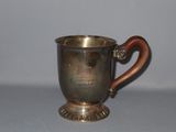 une tasse en argent avec un manche en bois posée sur une table