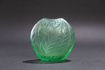 un vase en verre vert posé sur une table, sur fond noir