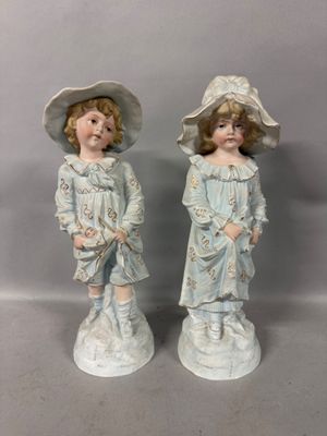 two figurines of two children wearing hats and holding flowers