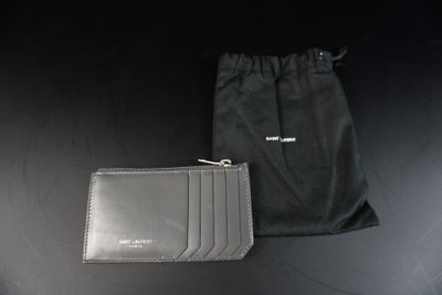 un portefeuille et une pochette en cuir noir posés sur une table noire, à côté d'un sac noir