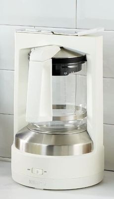 a white coffee maker sitting on a counter next to a cup