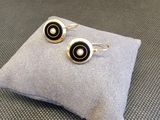 boucles d'oreilles argentées et noires posées sur un coussin, sur une surface grise