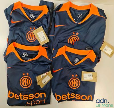 Deux t-shirts ornés de logos orange et bleus sont posés sur une table blanche