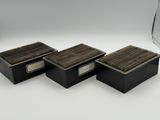 trois boîtes noires avec des couvercles en bois posées sur une surface blanche