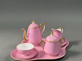 a pink tea set on a tray with a cup and saucer