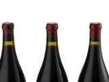 three bottles of red wine are lined up on a white surface
