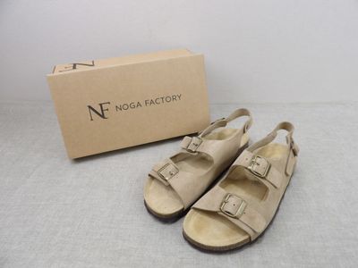 des sandales en cuir beige avec des boucles et un carton posé par terre