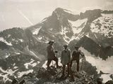 three men standing on top of a mountain with skis