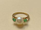 a close up of a pearl and emerald ring on a table