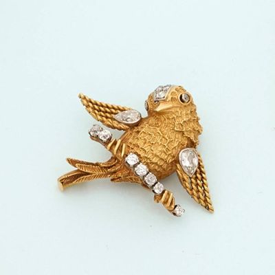 a gold bird brooch on a white surface