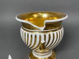 a white and gold vase with a gold spoon next to it