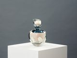 a glass bottle with a flower on top of a white pedestal