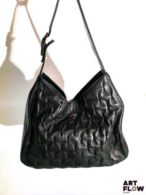 un sac à main en cuir noir suspendu à un crochet sur un mur blanc