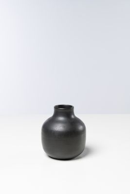 un vase noir posé sur une table blanche, avec un mur blanc en arrière-plan