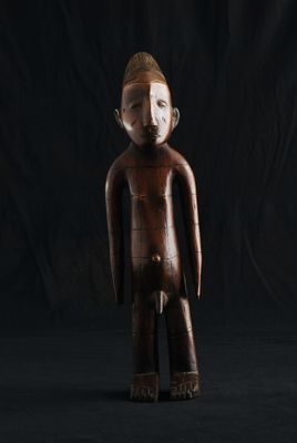 une statue en bois représentant un homme debout sur un fond noir
