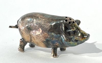 une petite figurine de cochon en métal posée sur une surface blanche