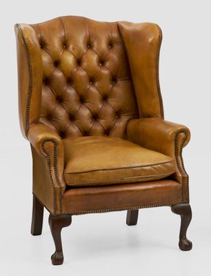 un fauteuil en cuir marron, avec un dossier capitonné et des pieds en bois
