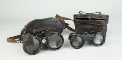 une paire de jumelles anciennes avec étui et courroie en cuir, sur fond blanc