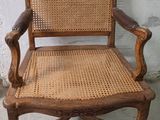 une vieille chaise en bois avec une assise en osier et des accoudoirs, adossée à un mur blanc