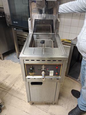 un homme debout à côté d'une friteuse dans une cuisine