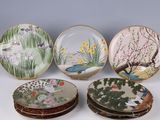four plates with birds and flowers painted on them sitting on a table