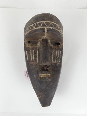 un vieux masque en bois accroché à un mur, sur une surface blanche