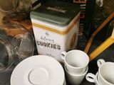 many cups and saucers on a table with a box of cookies in the background