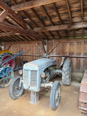 un vieux tracteur dans une grange, à côté d'autres machines agricoles