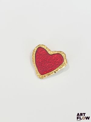 une broche en forme de cœur rouge, bordée d'or, sur fond blanc