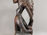 a wooden sculpture of a woman sitting on a stool