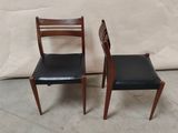 two wooden chairs with black leather seats sitting next to a white wall