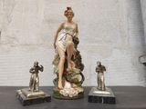 une statue représentant une femme assise sur une table, à côté d'autres statues
