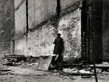 photographie en noir et blanc d'un homme debout devant un bâtiment en briques