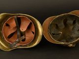 pair of antique brass helmets with leather linings on a black background
