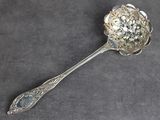 une cuillère ancienne en argent, ornée d'un motif floral sur un fond gris